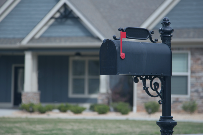 Black metal mailbox in front of a blue home.